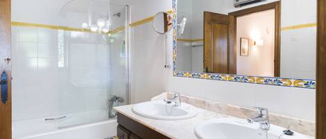 A bathroom with two sinks, a shower, and a large mirror with decorative tiles.