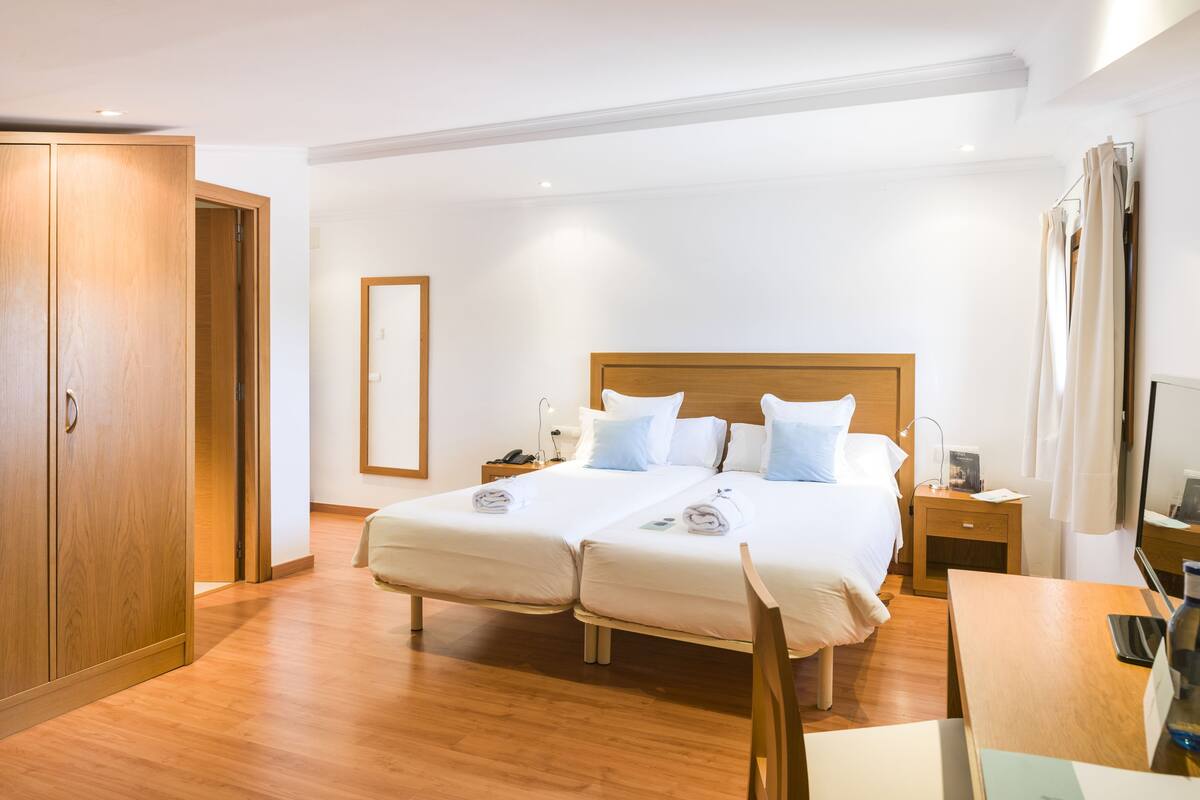 A double bed with a wooden headboard, two bedside tables, a chair, and a wooden wardrobe.