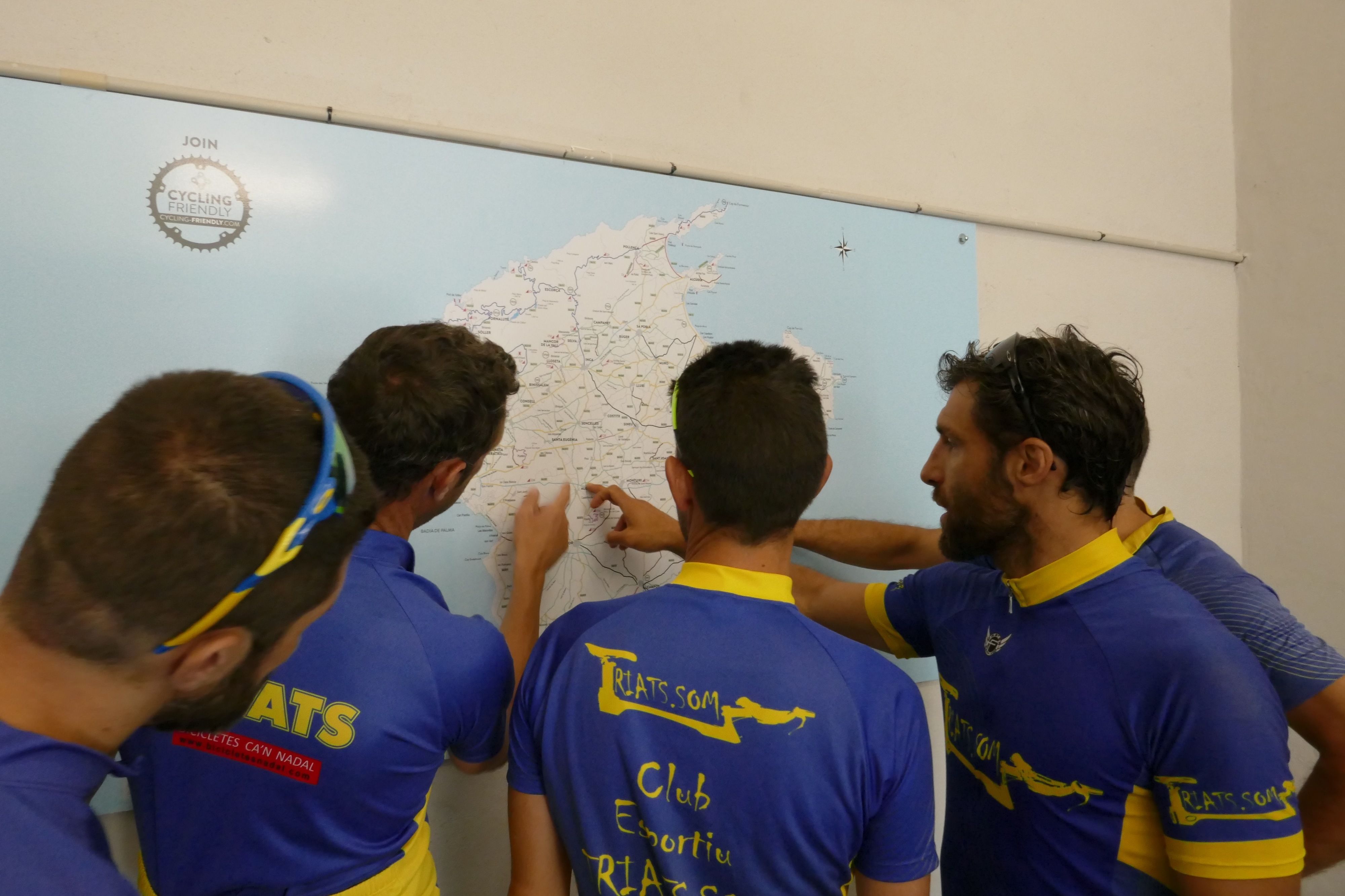 Cuatro personas con camisetas de equipo ciclista en azul y amarillo, reunidas alrededor de un mapa.