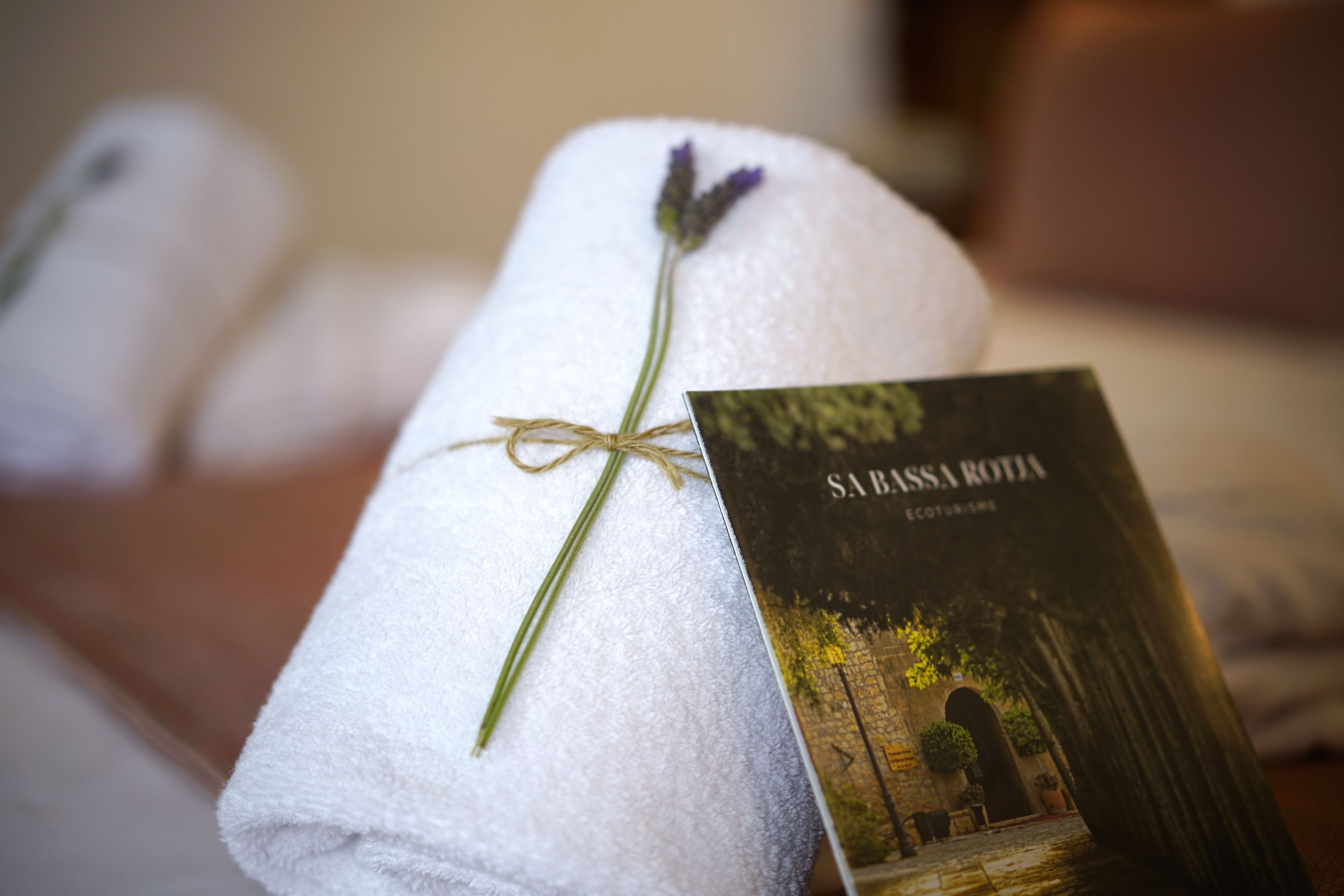 A neatly folded white towel with a lavender sprig tied with twine, placed next to a booklet titled 'SABBA ROTA ECO TOURISM'.