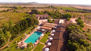 Vue aérienne d’un complexe hôtelier doté d’une piscine, de chaises longues et d’une grande villa avec un toit en tuiles.