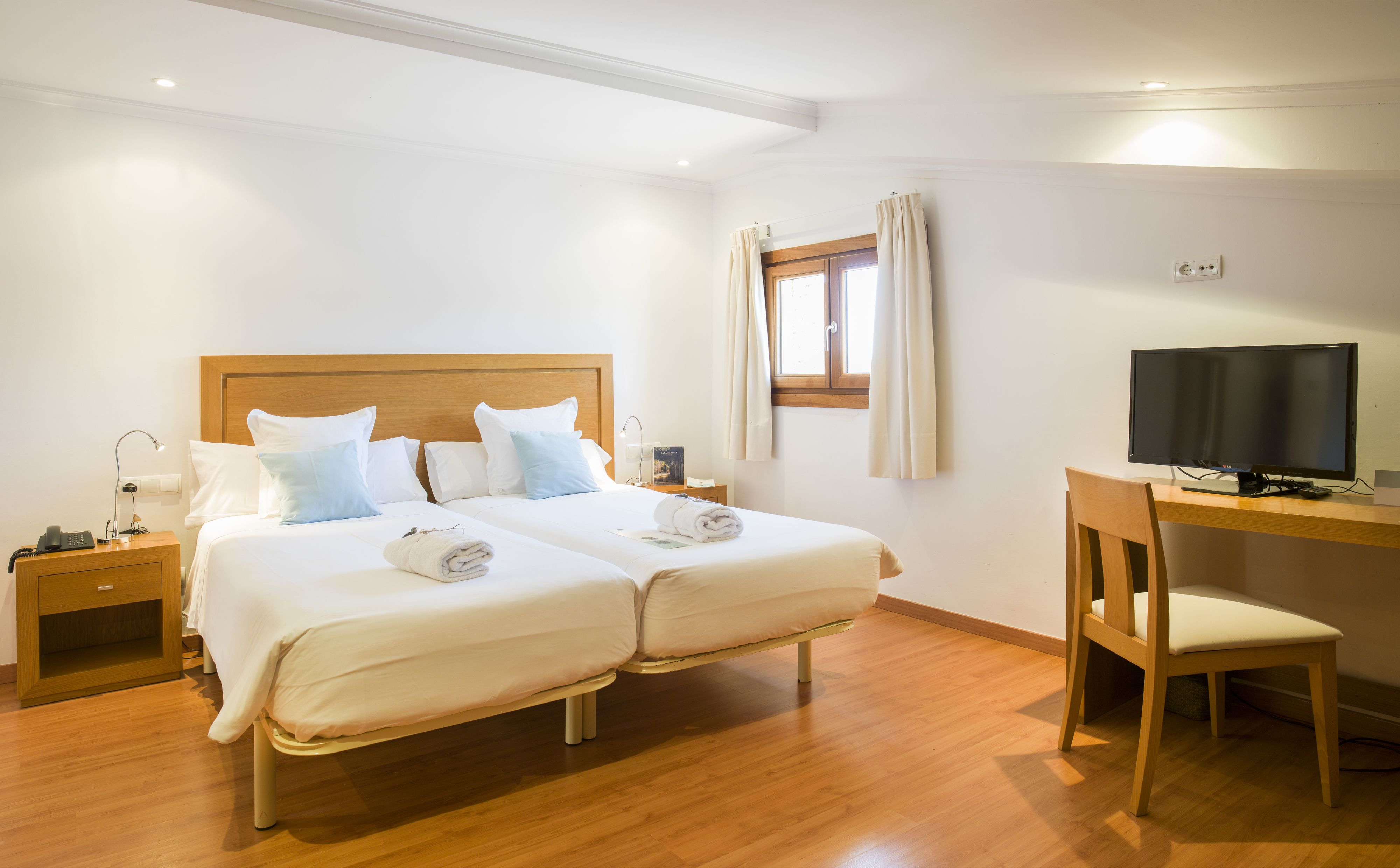 A hotel room with two beds, a desk with a TV, a chair, a nightstand with a phone, and a window with curtains.