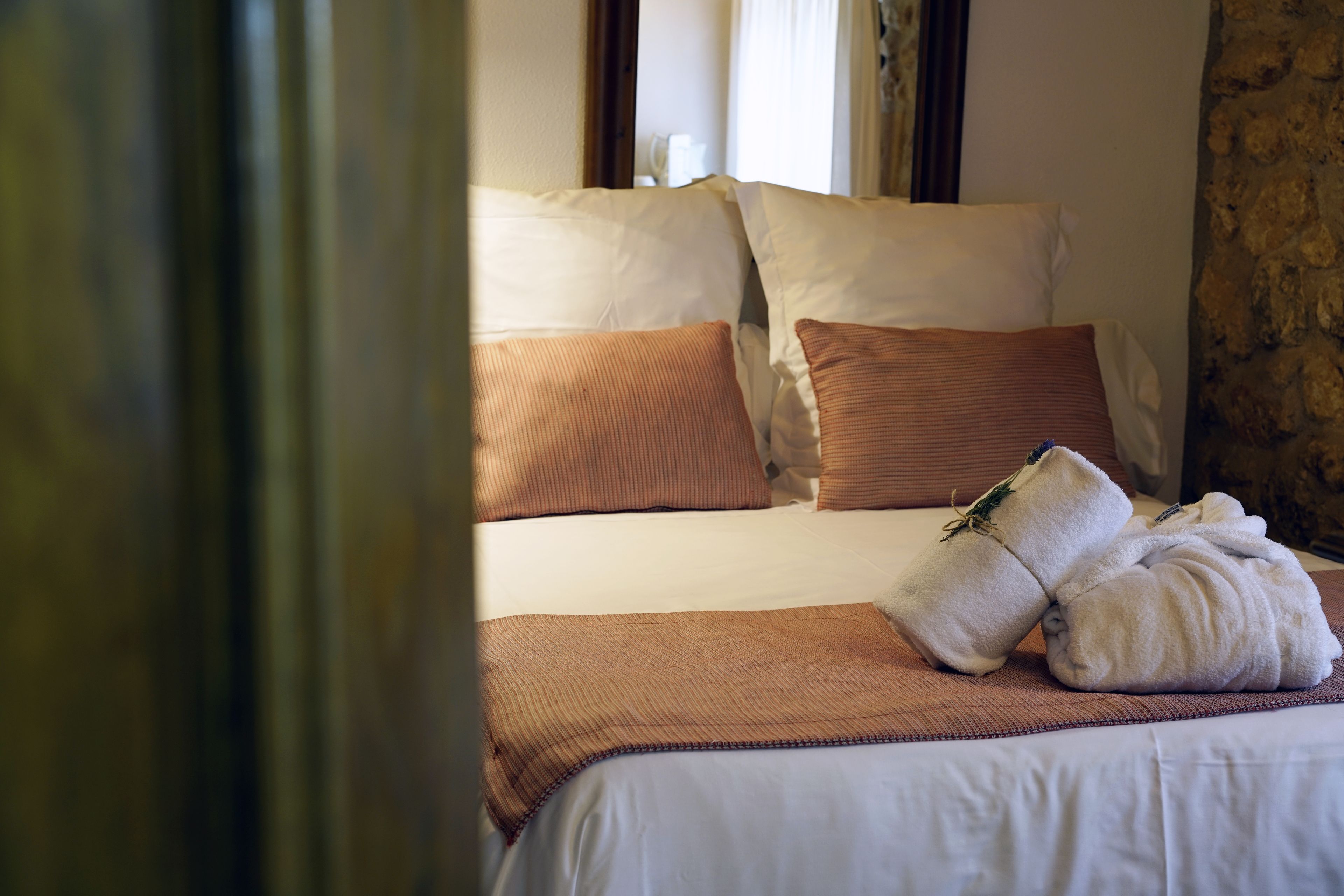 Una cama bien hecha con ropa de cama blanca y marrón, una toalla doblada y una manta marrón.