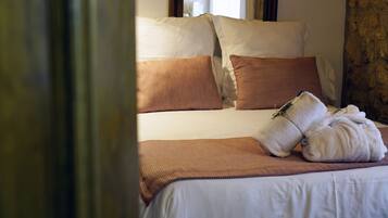 Una cama bien hecha con ropa de cama blanca y marrón, una toalla doblada y una manta marrón.