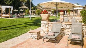 Un espace aménagé au bord de la piscine, avec des chaises longues, des parasols et un mur en pierre agrémenté de jardinières.