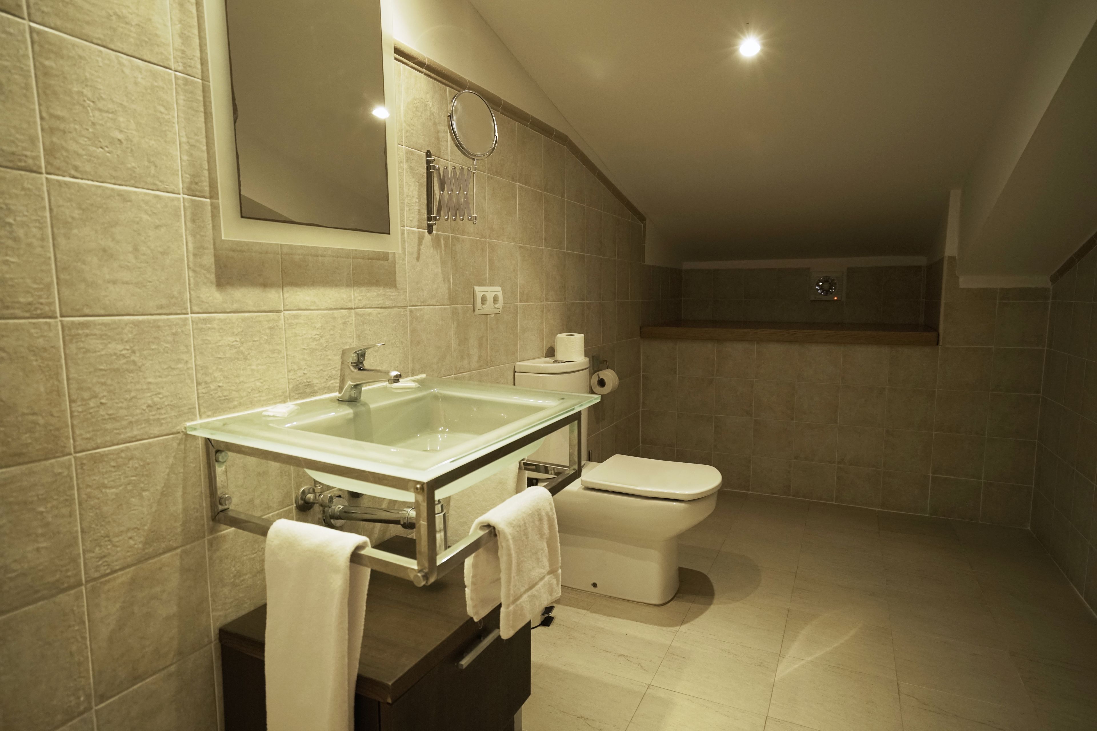 Een moderne badkamer met een glazen wastafel, toilet en ligbad.