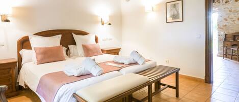 A hotel room with a large bed, a bench, and a desk.