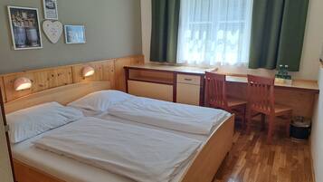 A room with a wooden bed, a desk, and a chair. There are pictures on the wall and a window with curtains.