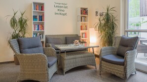 Un rincón acogedor para leer, con mobiliario de mimbre, una mesa de centro de cristal y estanterías llenas de libros.