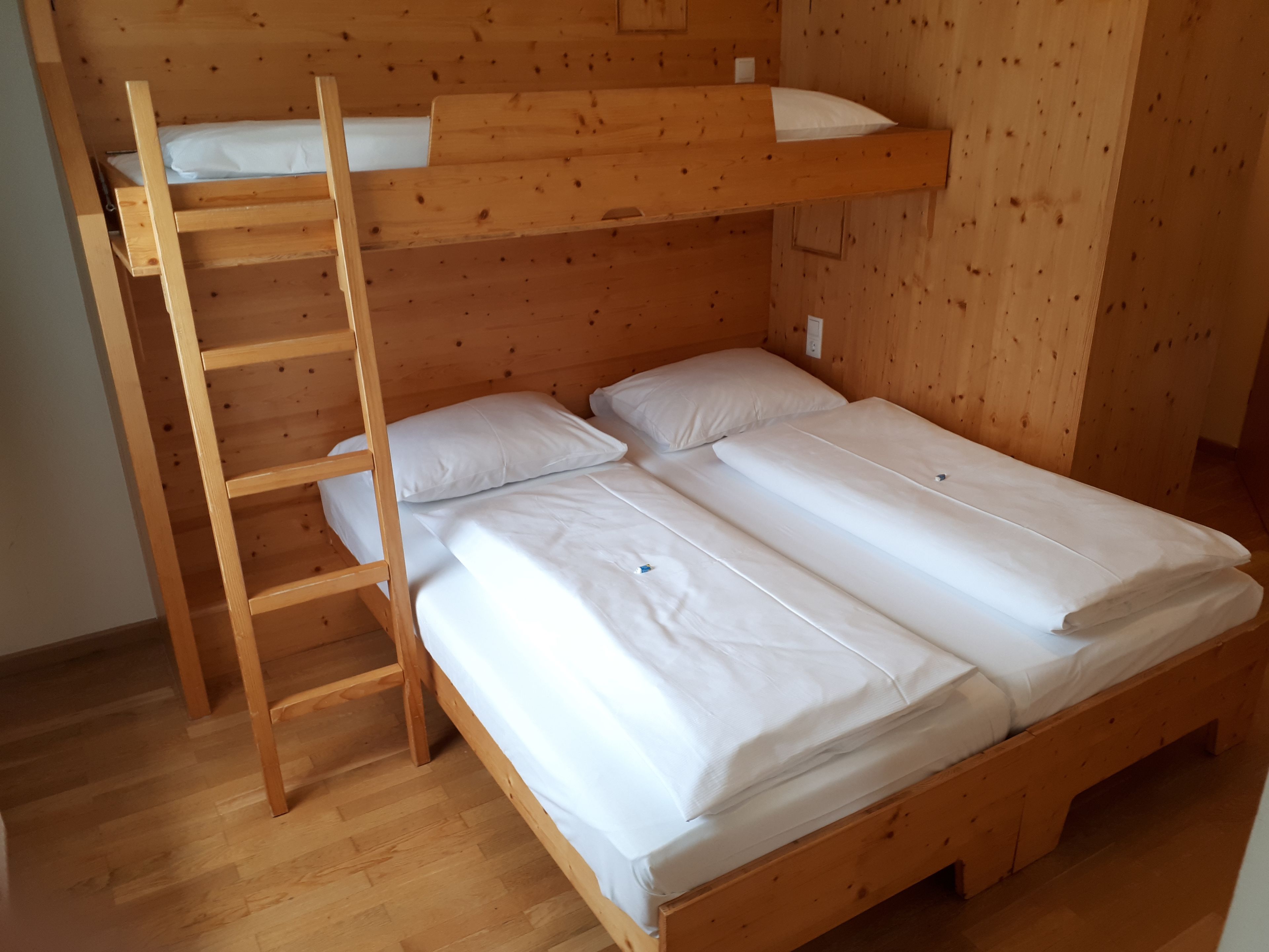 A bunk bed with a wooden ladder, white bedding, and a wooden wall.