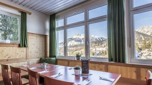 Una mesa de madera con sillas, un banco y vistas a montañas a través de amplios ventanales.