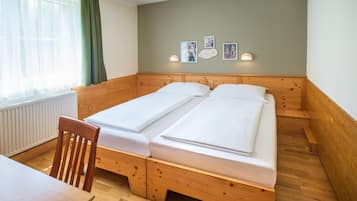 A room with two wooden beds, a wooden chair, a table, and a window with curtains.