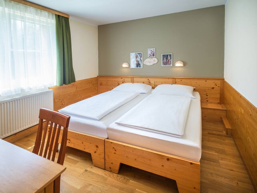 A room with two wooden beds, a wooden chair, a table, and a window with curtains.