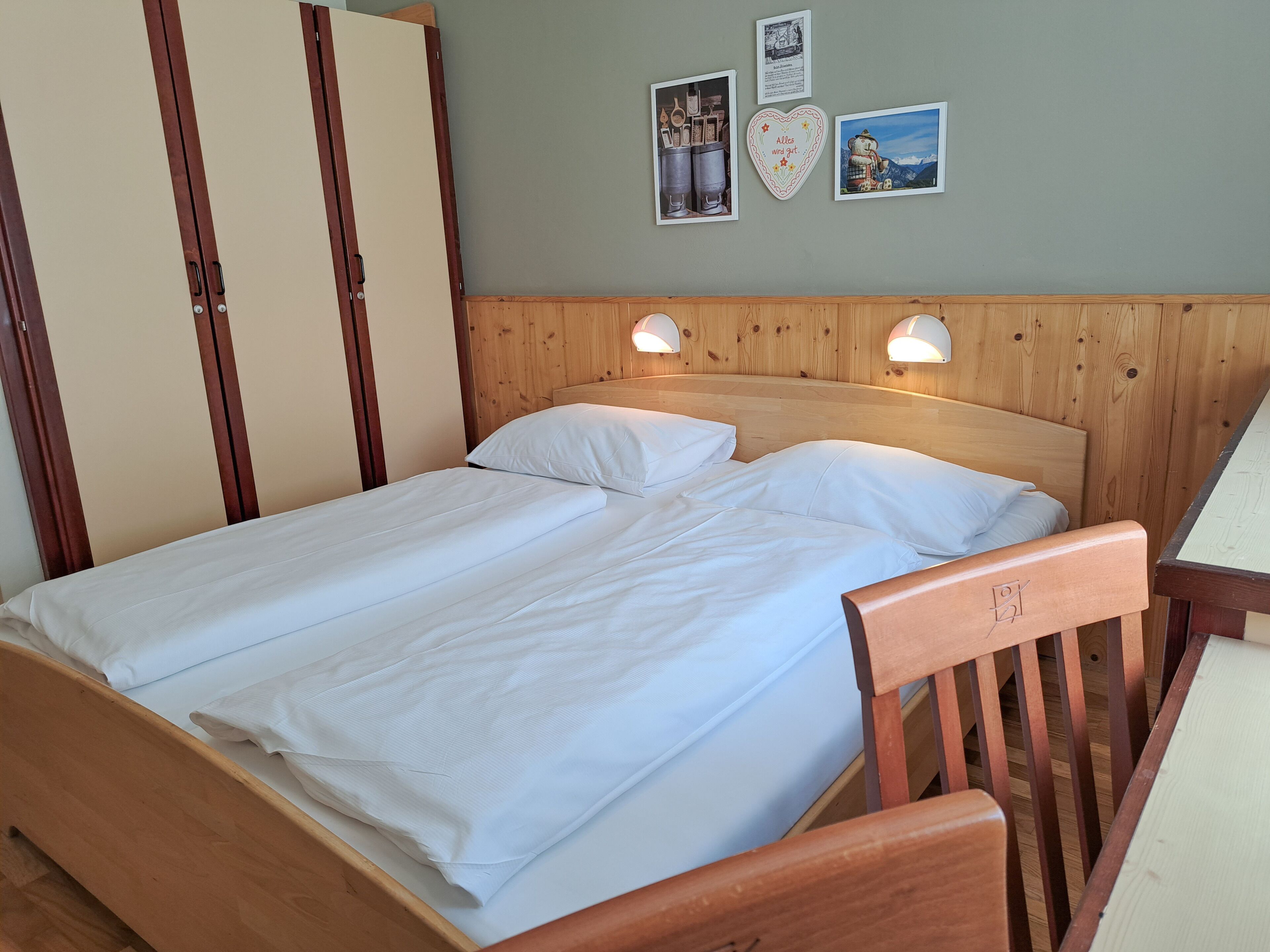 A wooden bed with two white pillows and a wooden headboard. There are two wall-mounted lamps on either side of the bed.