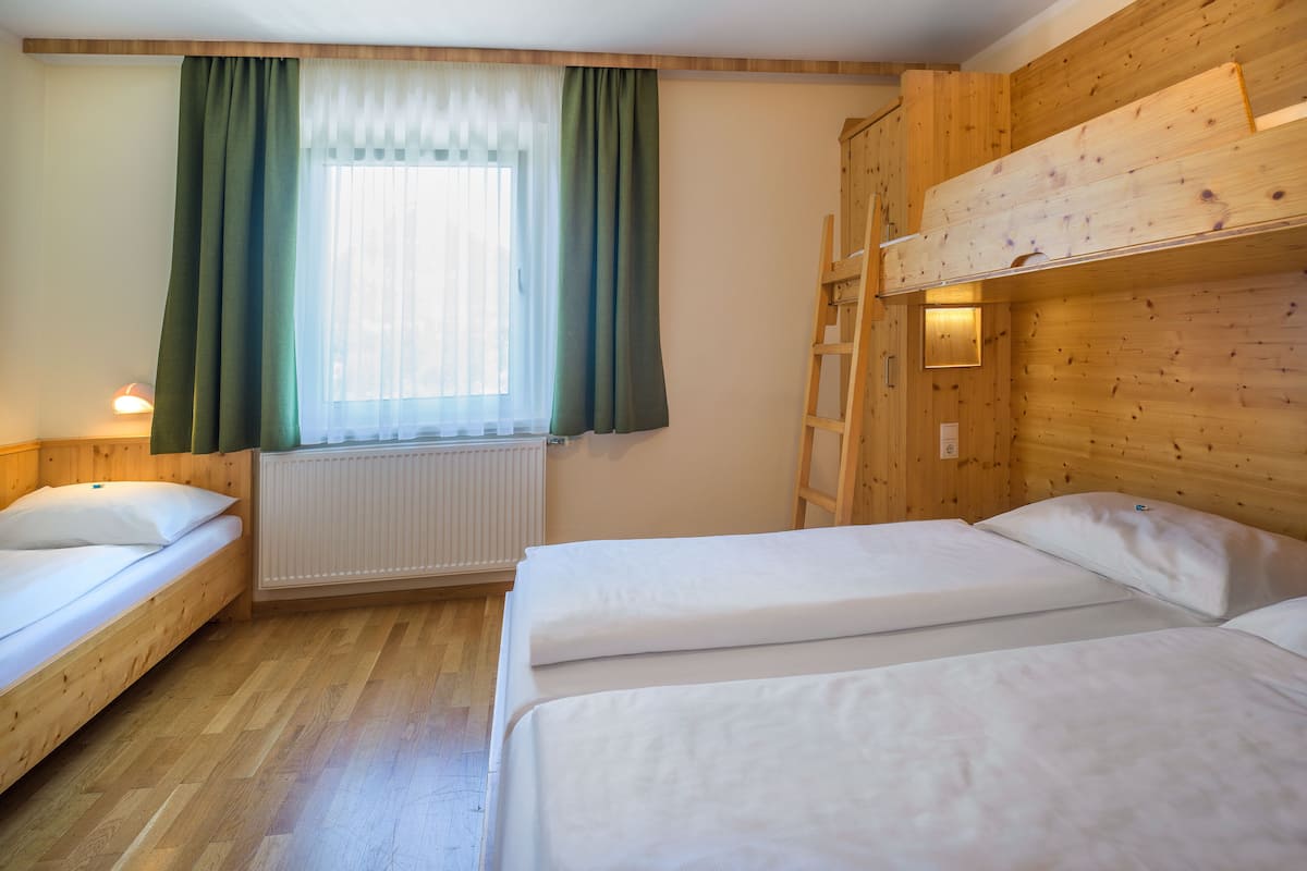 Een kamer met twee eenpersoonsbedden, een raam met gordijnen, een radiator en houten wanden.
