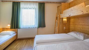 Ein Zimmer mit zwei Einzelbetten, einem fenster mit Vorhängen, einem Heizkörper und Holzwänden.