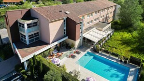 A multi-story hotel with a swimming pool, outdoor seating, and a view of the surrounding landscape. - Ibis Golfe de Saint Tropez (Cogolin)