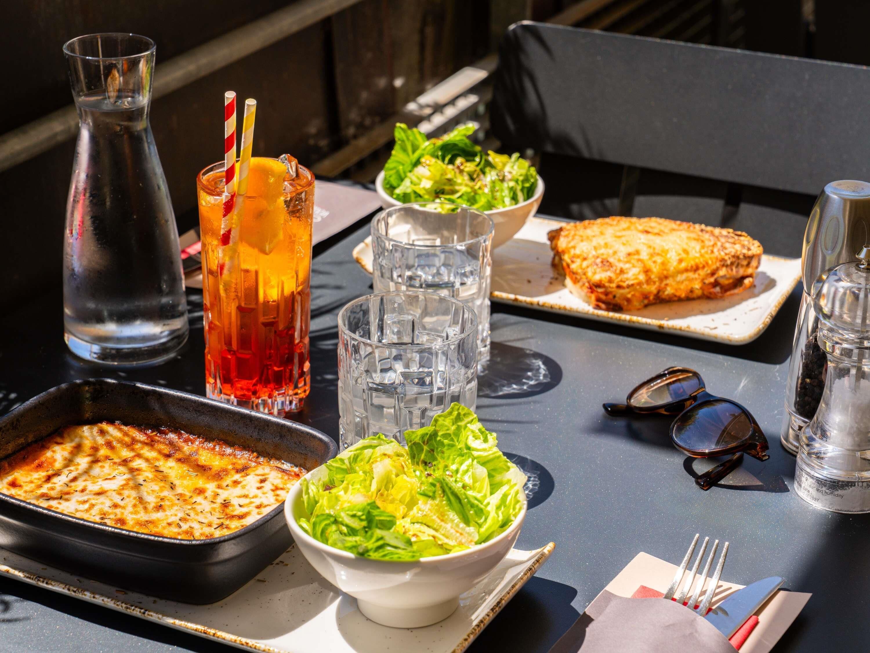 Een tafel met een bord, salade, drankjes en een pan.