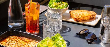 Een tafel met een bord, salade, drankjes en een pan.
