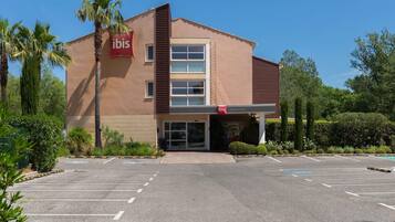 A modern building with a 'ibis' sign, a parking lot, and surrounding greenery.