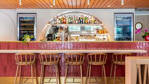 A bar area with a curved counter, stools, and a variety of bottles and glasses. - Ibis Golfe de Saint Tropez (Cogolin)