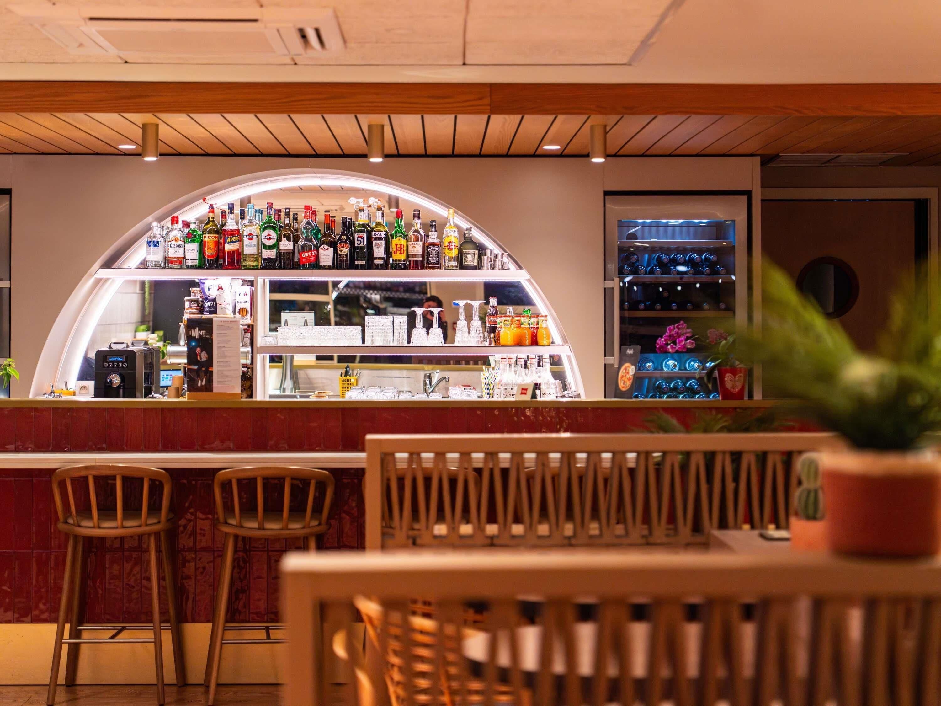 Un espace bar doté d’un comptoir incurvé, de différentes bouteilles et d’un coin salon avec des chaises en bois.