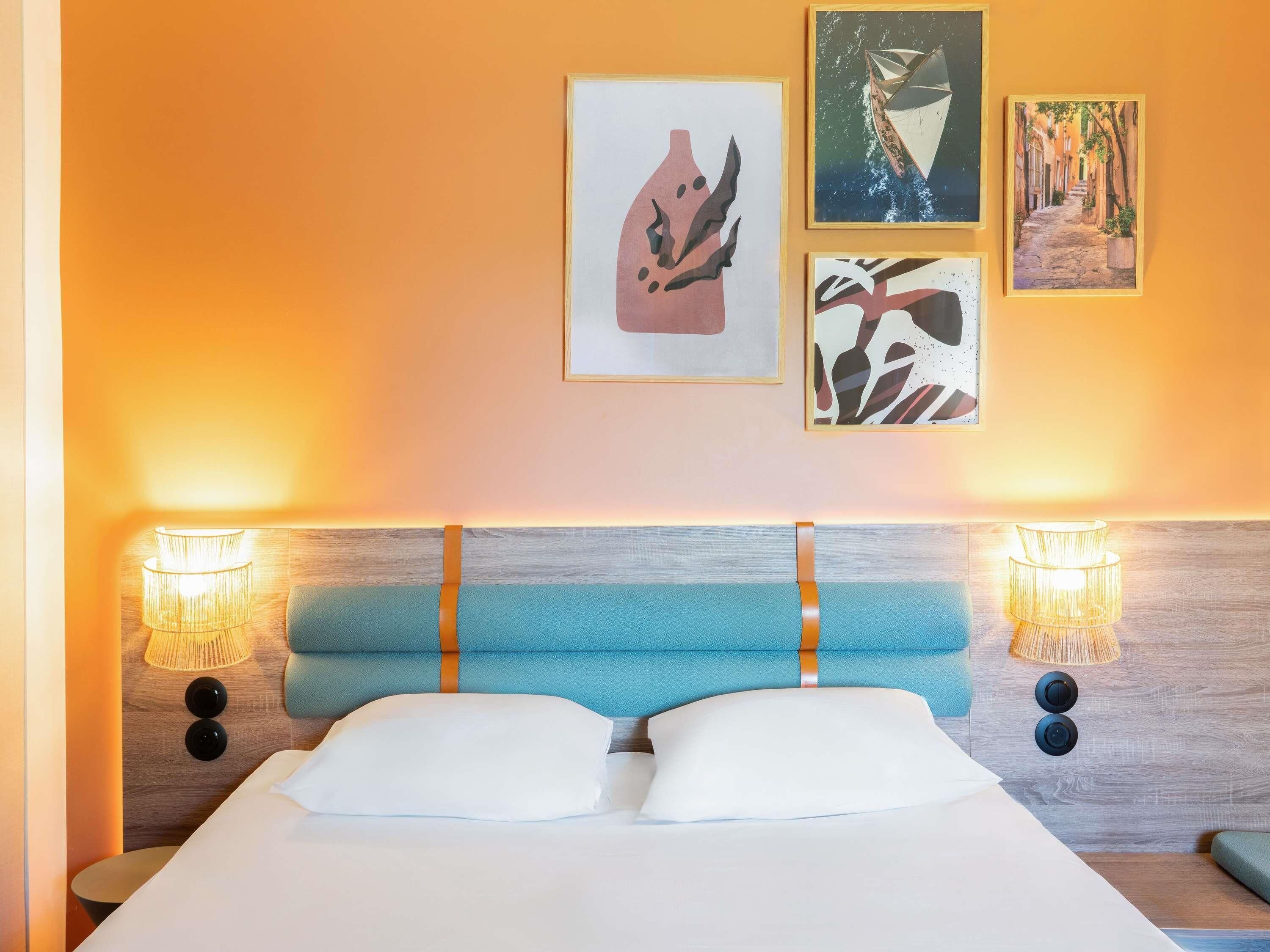 A bed with a blue headboard, two wall-mounted lamps, and three framed artworks on the wall.