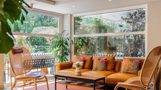 A cozy living area with a sofa, chairs, a coffee table, and large windows offering a view of greenery. - Ibis Golfe de Saint Tropez (Cogolin)
