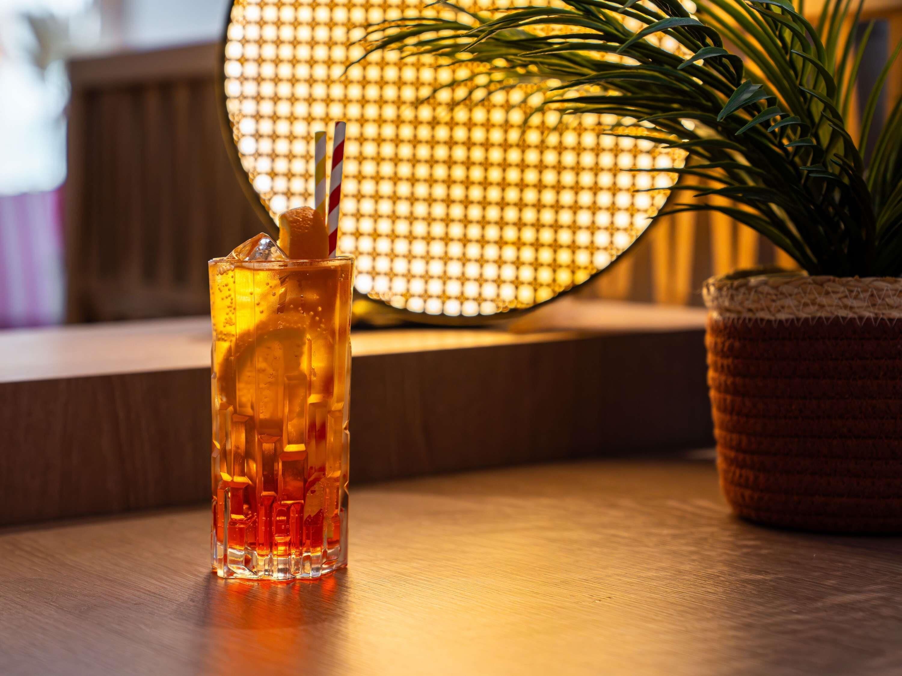 Ein Glas mit Stroh auf einer Holzoberfläche, eine Topfpflanze und eine Wand mit Muster im Hintergrund.