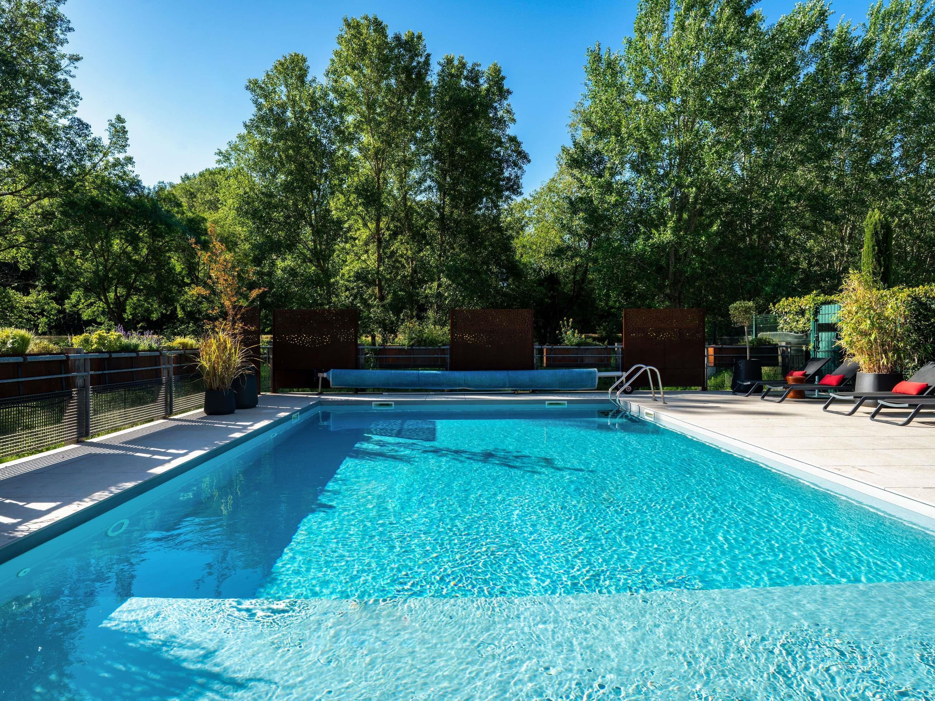 A rectangular swimming pool with clear blue water, surrounded by a deck with lounge chairs and potted plants.