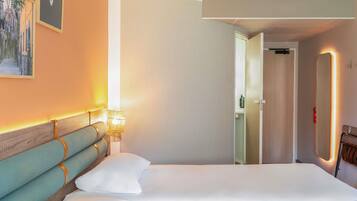 Une chambre d’hôtel avec un grand lit, une tête de lit en bois, une lampe fixée au mur et une porte donnant sur une autre pièce.