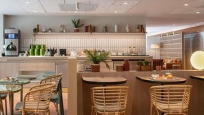 A modern restaurant with a central island, wicker chairs, and a variety of plants and kitchen appliances. - Ibis Golfe de Saint Tropez (Cogolin)
