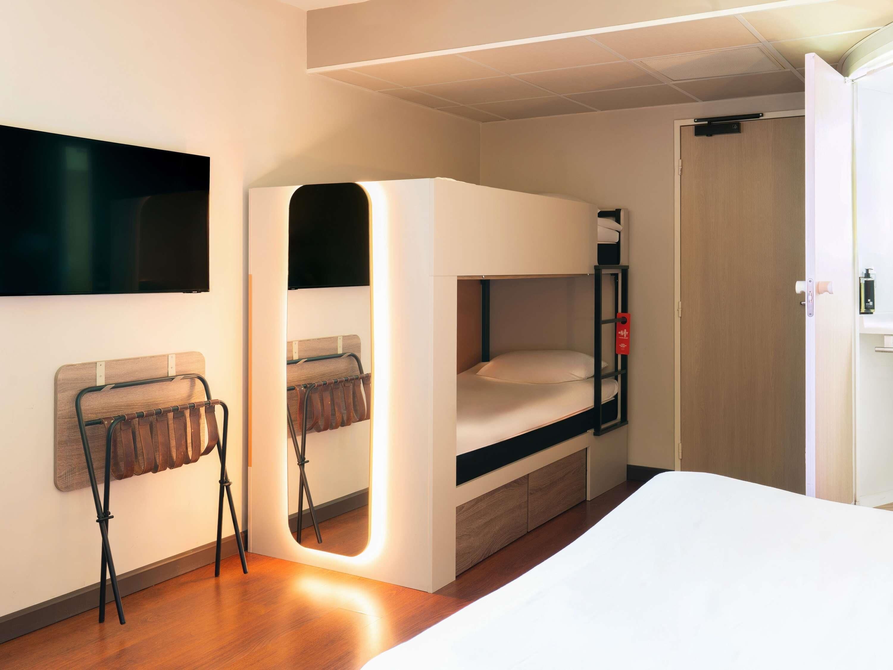 Una cama litera con un espejo, una silla y un televisor montado en la pared.