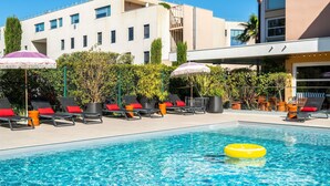 A swimming pool with lounge chairs and umbrellas, surrounded by greenery and buildings. - Ibis Golfe de Saint Tropez (Cogolin)