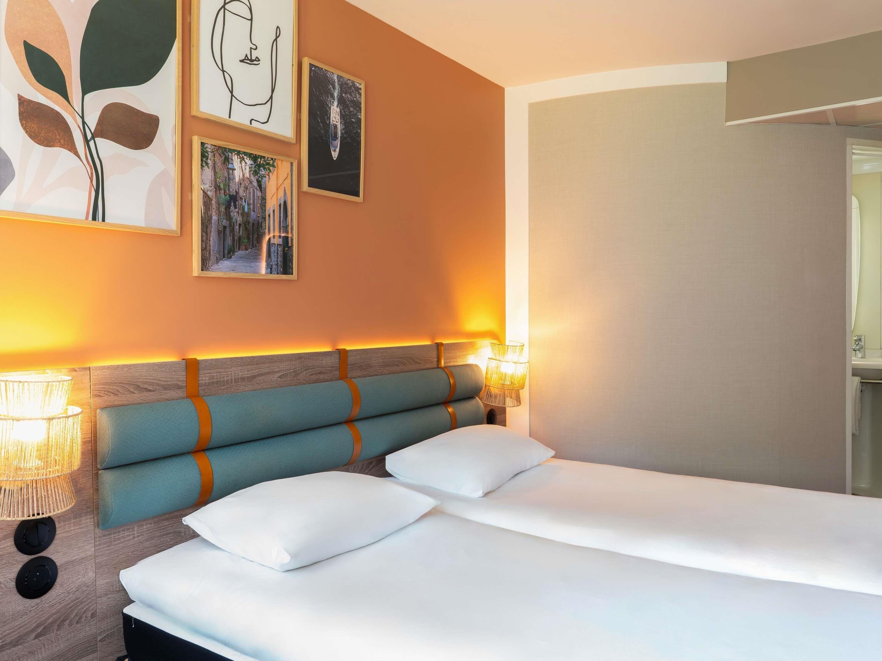 Ein Hotelzimmer mit einem Bett, zwei Kissen, einem Kopfteil mit Holzpaneelen und an der Wand befestigter Kunst.