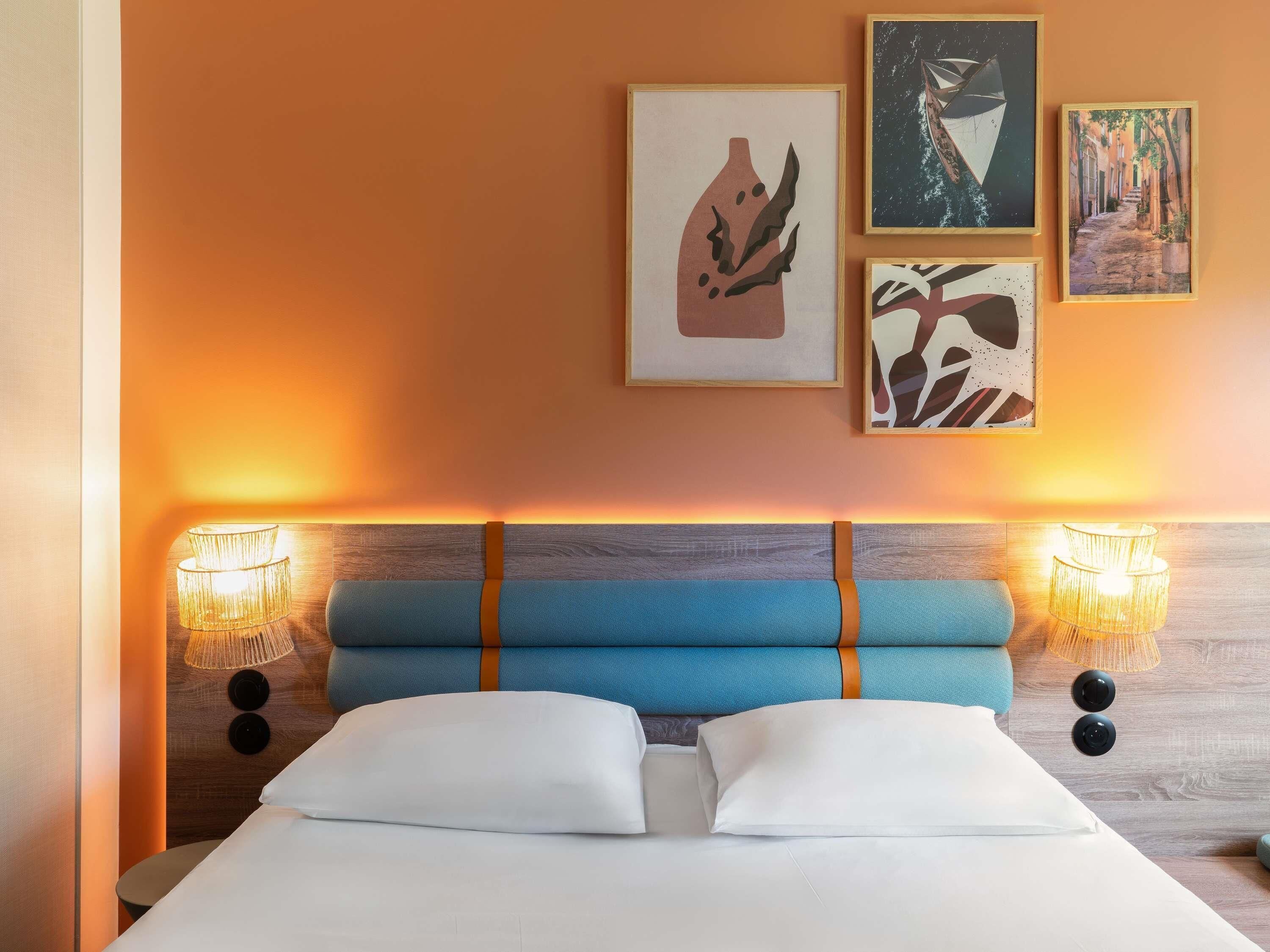 Ein Hotelzimmer mit einem Bett, zwei Wandlampen und drei gerahmten Kunstwerken.