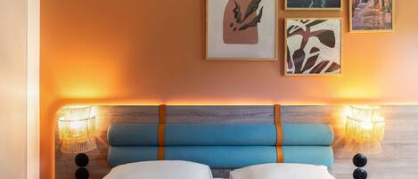 A hotel room with a bed, two wall-mounted lamps, and three framed artworks.