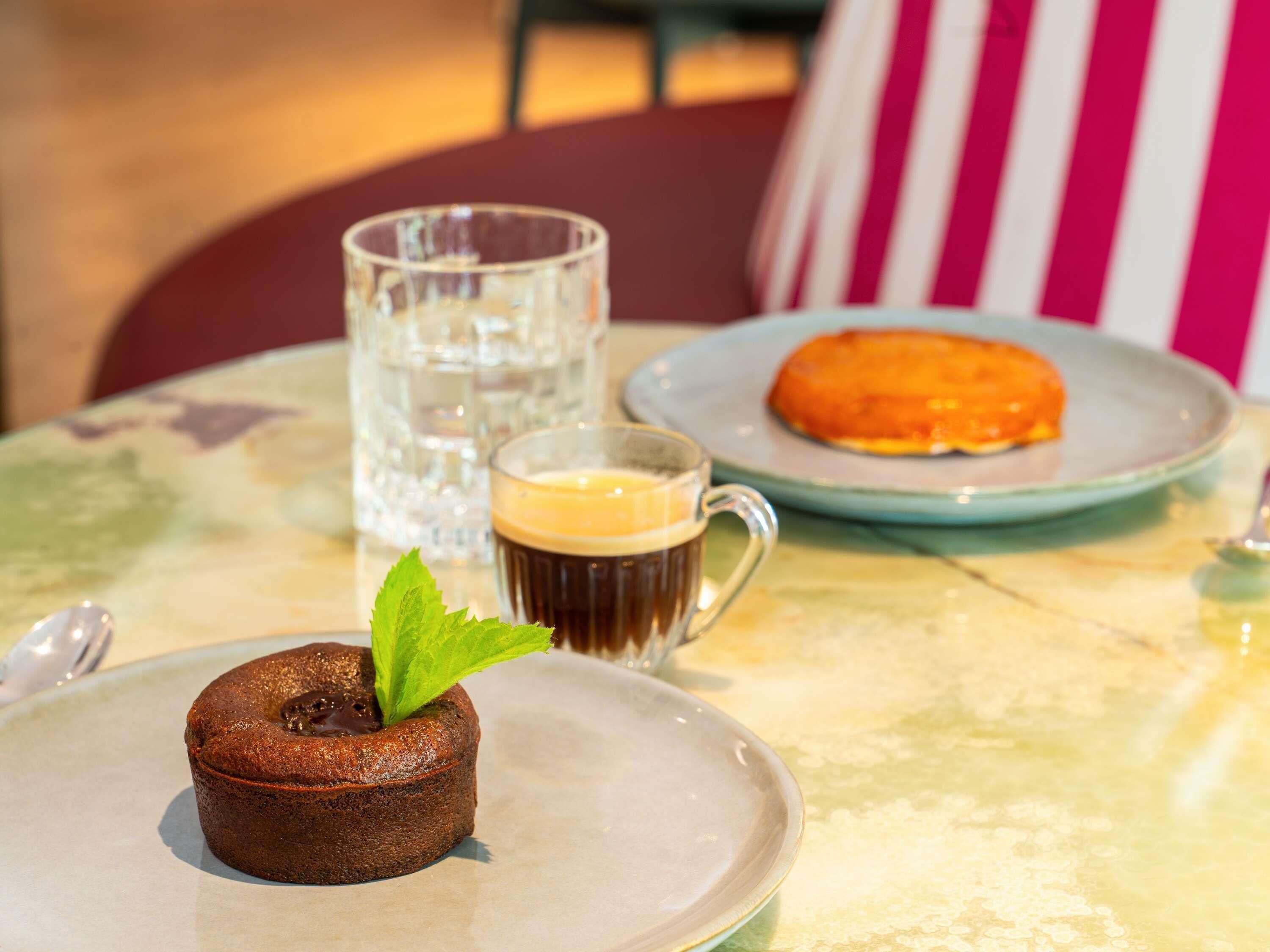 A dessert plate with a chocolate cake, a glass of coffee, and a plate with a pastry.
