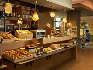 Una barra de desayuno con diversos pasteles, una máquina de café y lámparas colgantes.