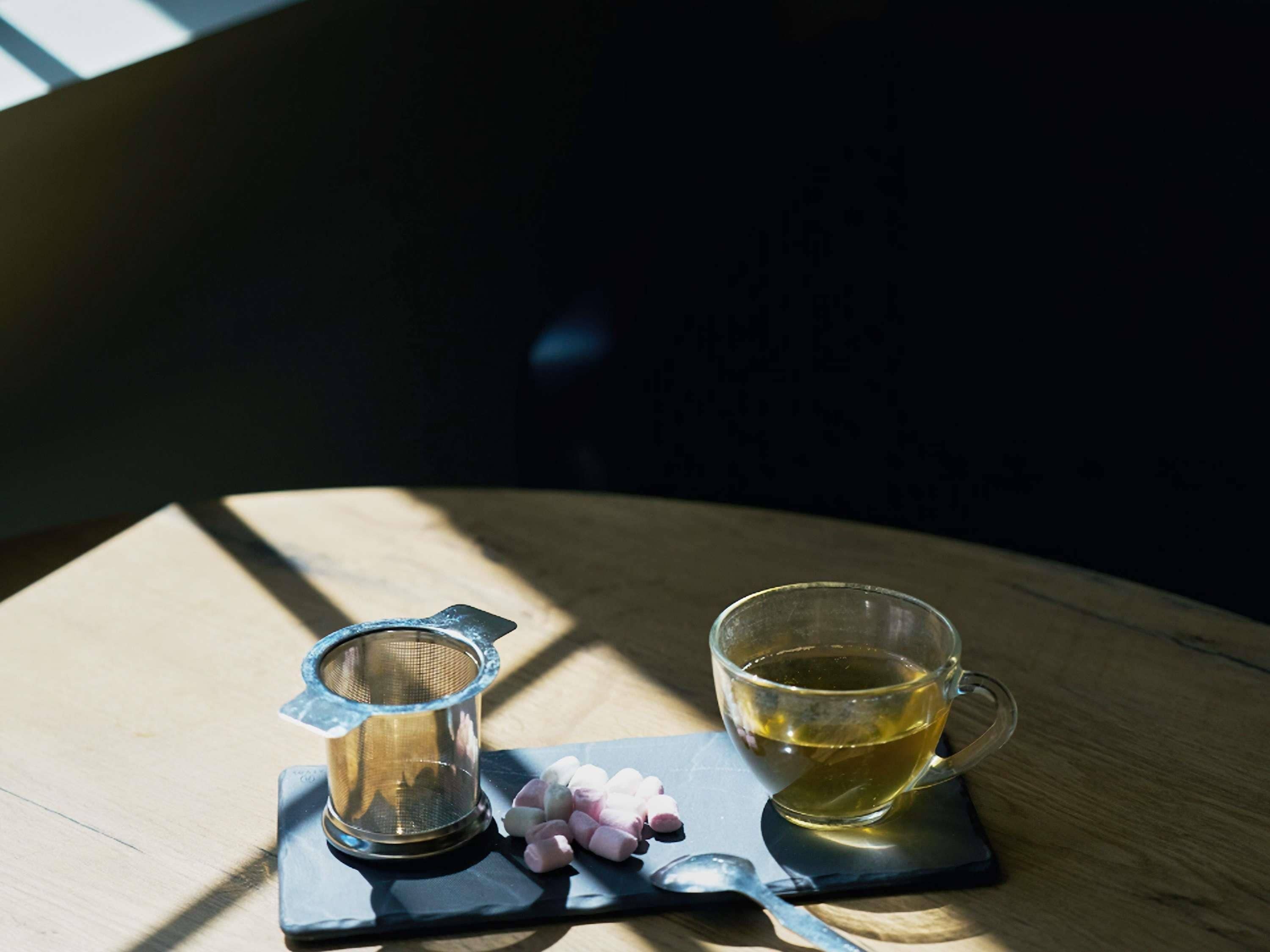A wooden table with a tea set, including a teapot and cup, and a small container of marshmallows.