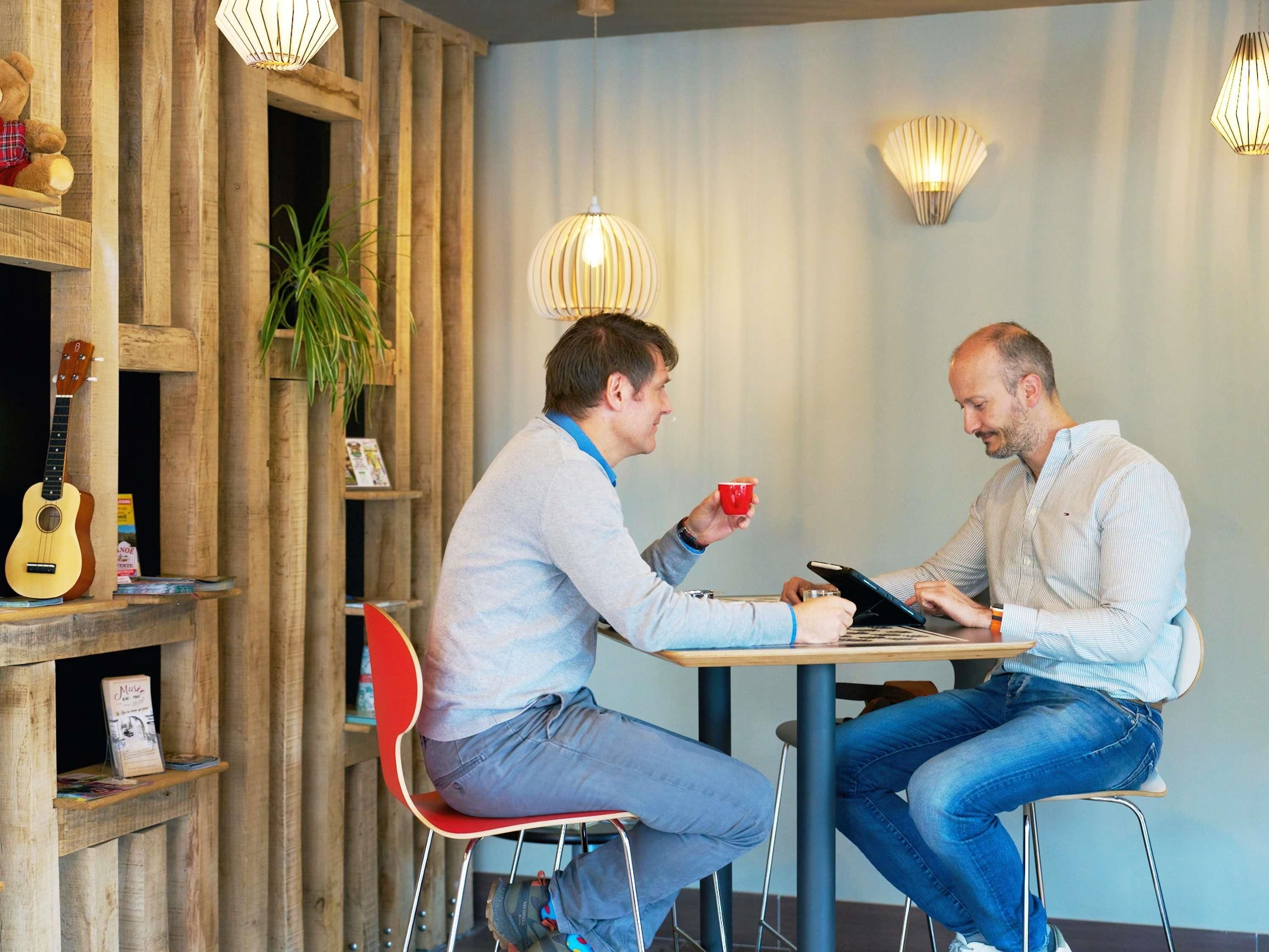Dos personas sentadas en una mesa en una habitación con paneles de madera e iluminación colgante.