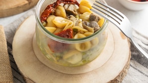 Un frasco de vidrio con pasta, tomates secos al sol y aceitunas sobre una tabla de madera.