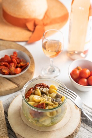 A glass jar of pasta with sun-dried tomatoes and olives on a wooden board. - ibis Sarlat (Sarlat-la-Canéda)