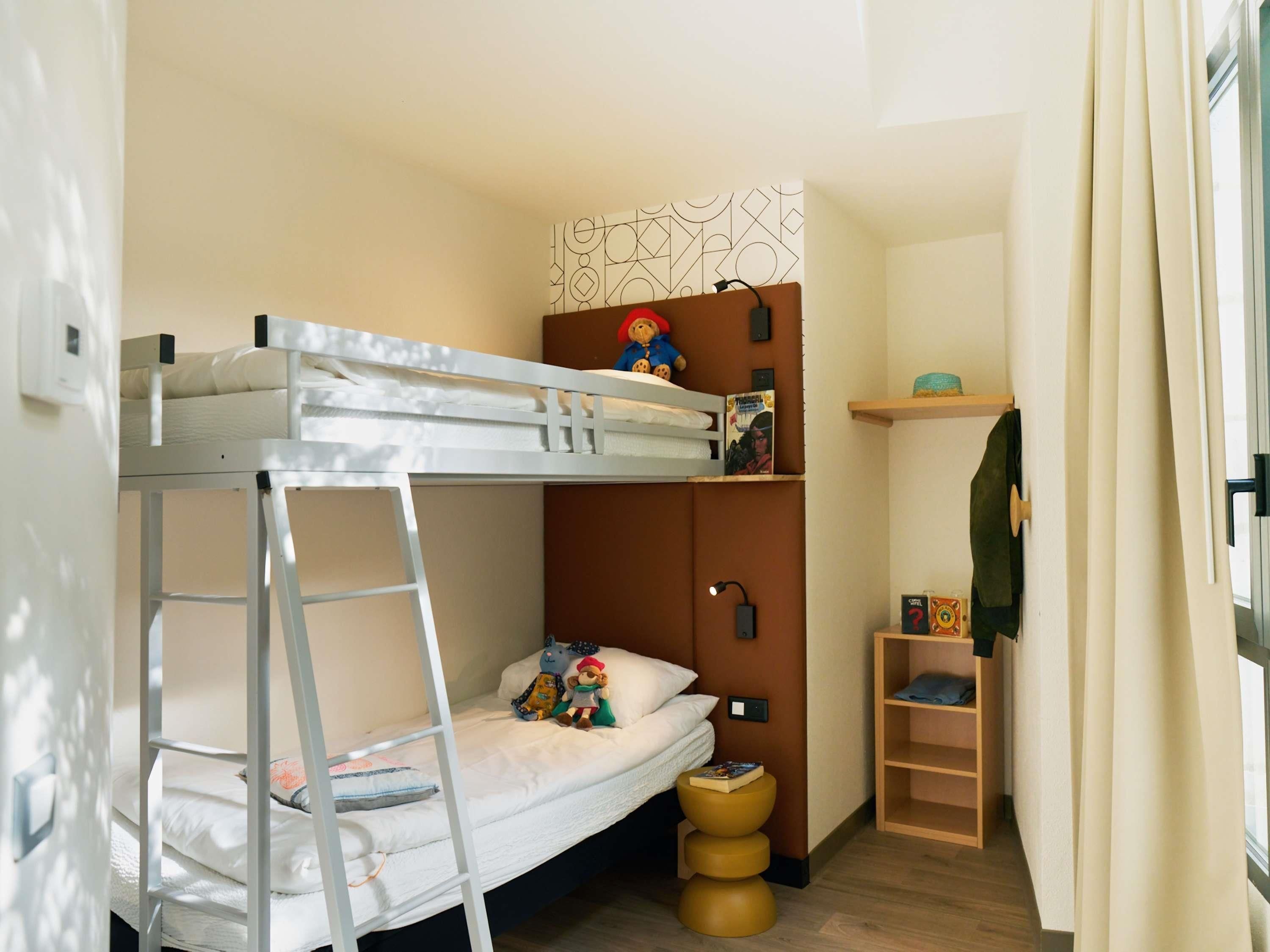 A bunk bed with a ladder, a small shelf with books, and a wooden ladder shelf.