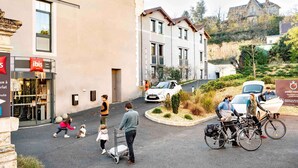 A hotel entrance with a sign for 'ibis HOTEL' and a parking area with a white car and bicycles. - ibis Sarlat (Sarlat-la-Canéda)