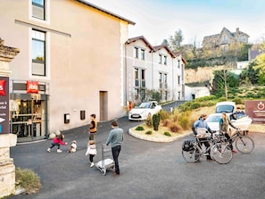 A hotel entrance with a sign for 'ibis HOTEL' and a parking area with a white car and bicycles. - ibis Sarlat (Sarlat-la-Canéda)