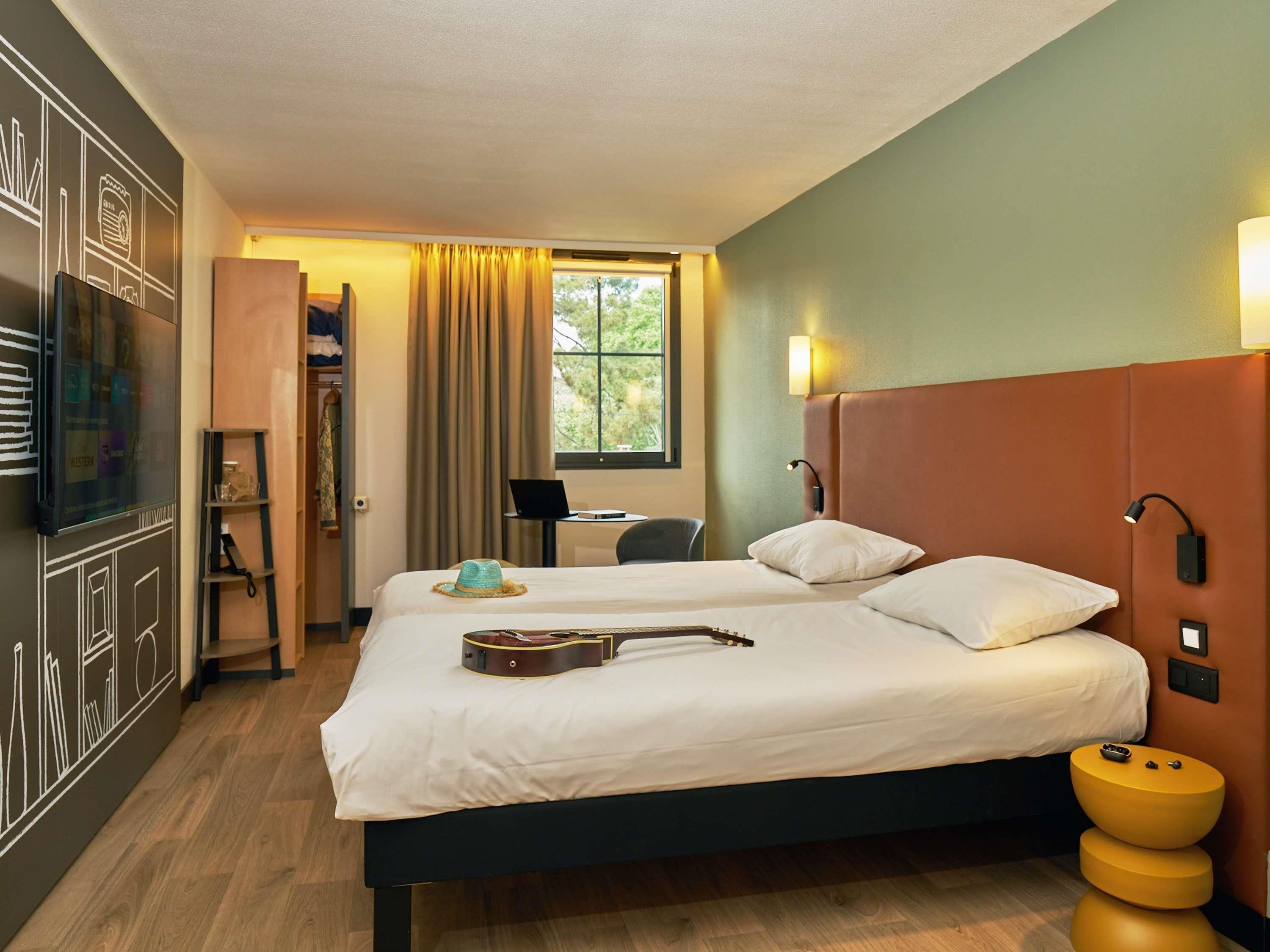 Habitación de hotel con cama, una guitarra, una laptop y un escritorio con silla.
