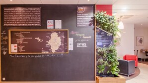 A hotel reception area with a blackboard displaying various information, including a map and a list of amenities. - ibis Sarlat (Sarlat-la-Canéda)