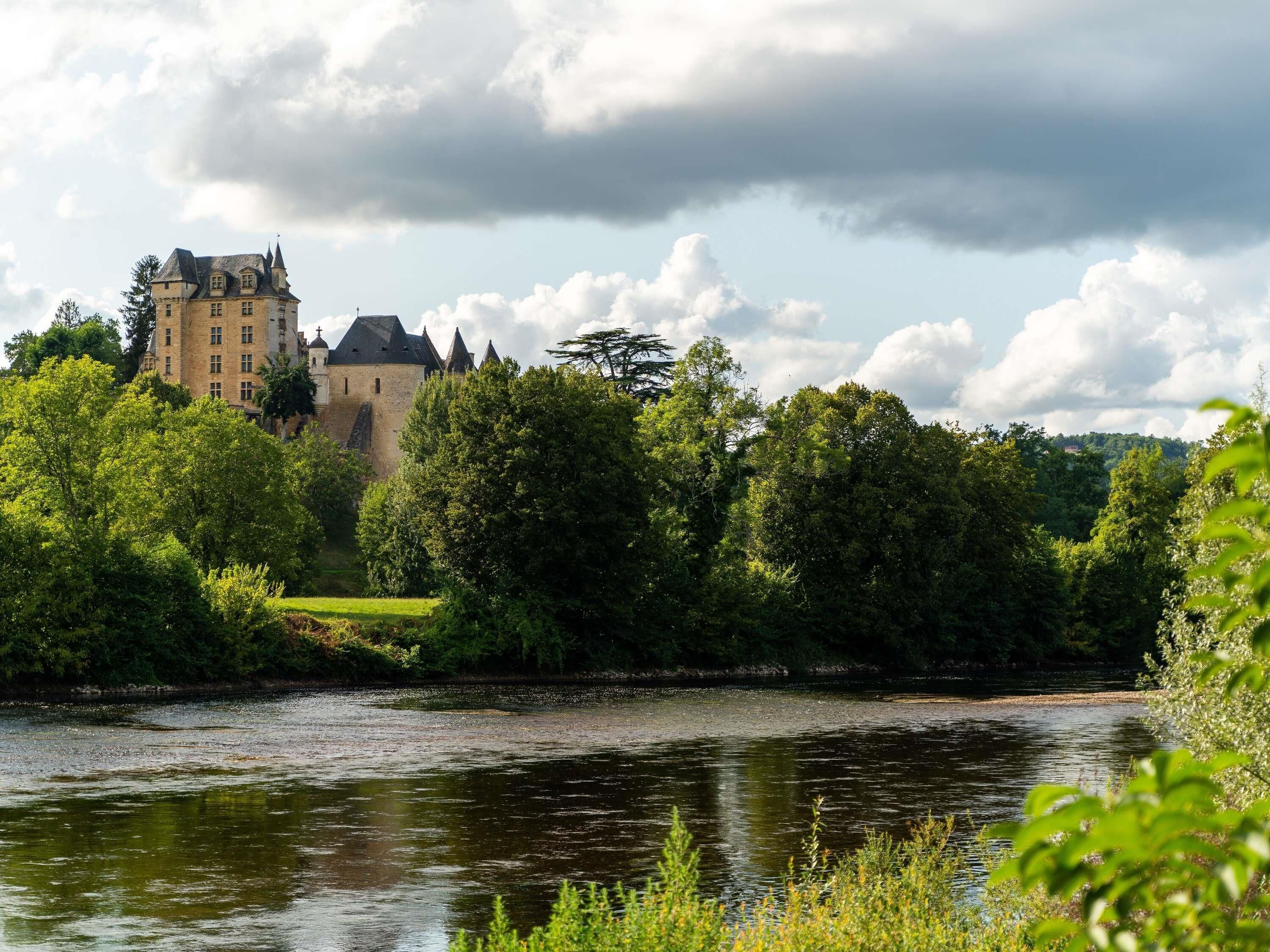 Un château entouré d’une végétation luxuriante et bordé par une rivière.