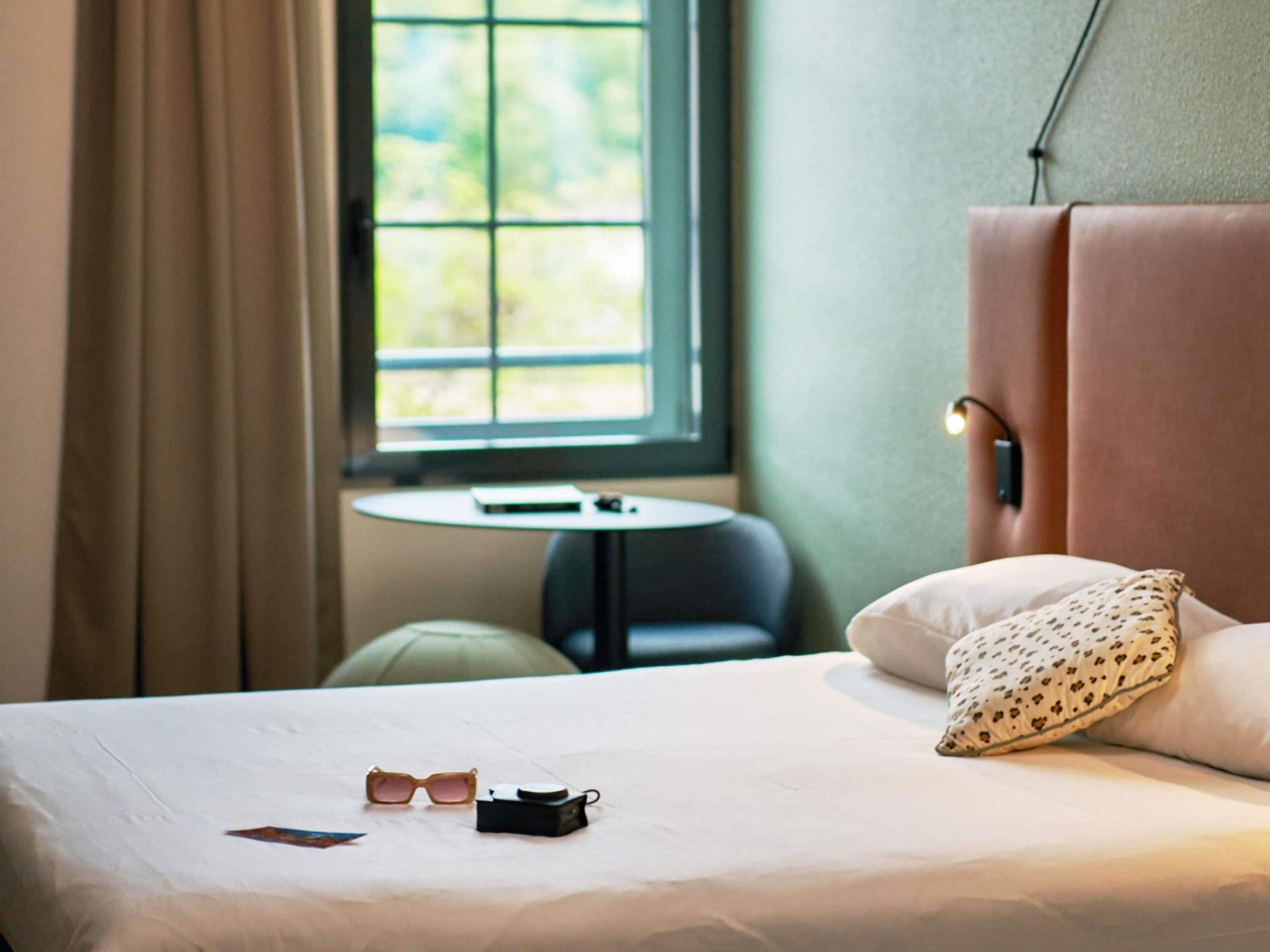 Een hotelkamer met een bed, een klein tafeltje en een raam met gordijnen.
